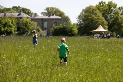 Børn løber over en græsmark hen mod et gods med en tipi-pavillon i baggrunden