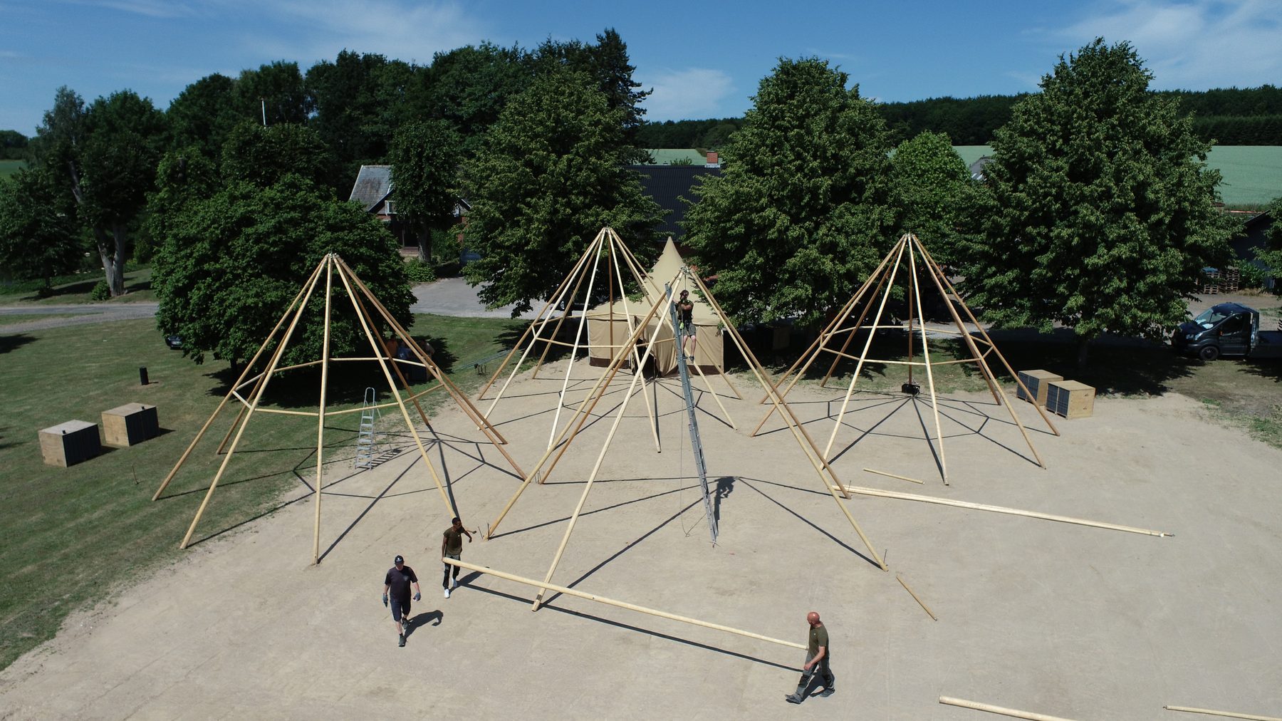 Luftfoto af tre tipi-stangsæt under opsætning på en åben plads