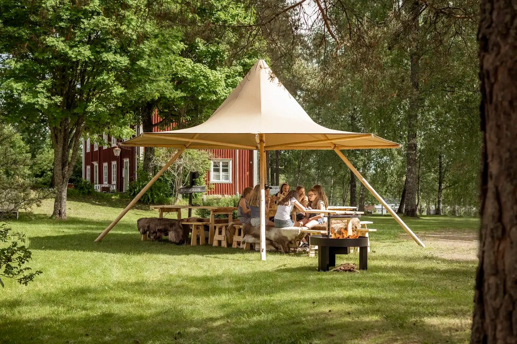 Tipi-pavillon på en grøn plæne foran et rødt hus